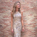 Model wearing a sleeveless champagne and silver floral sequin midi dress against a brick wall