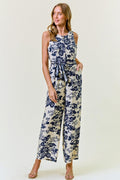 Model wearing a navy and cream floral print sleeveless wide-leg jumpsuit with tie-waist belt