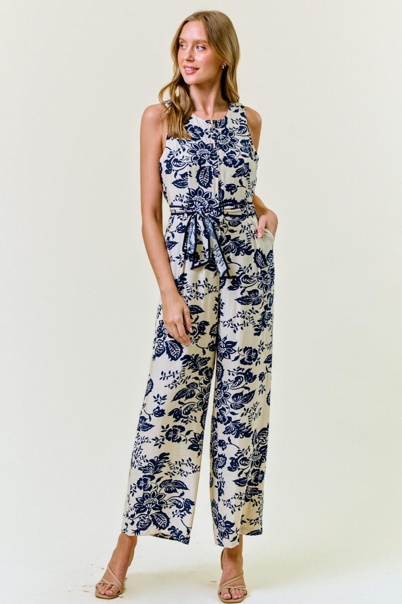 Model wearing a navy and cream floral print sleeveless wide-leg jumpsuit with tie-waist belt